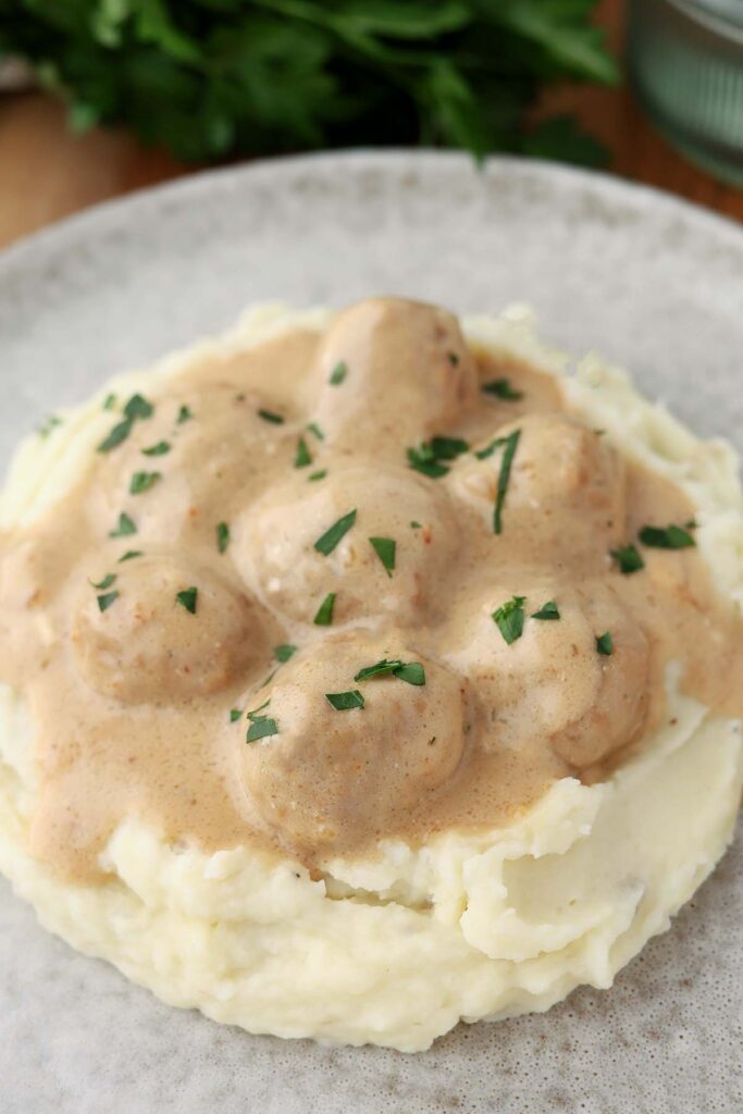 close up image sowing a gray plate topped with mashed potatoes and meatballs in a light brown gravy