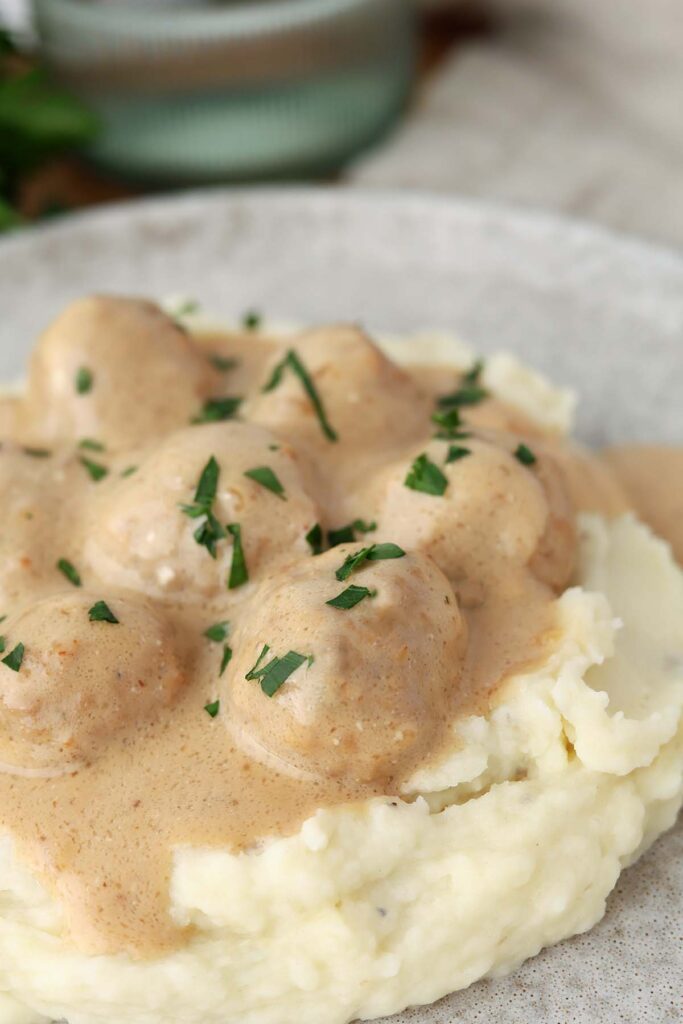 close up image sowing a gray plate topped with mashed potatoes and meatballs in a light brown gravy
