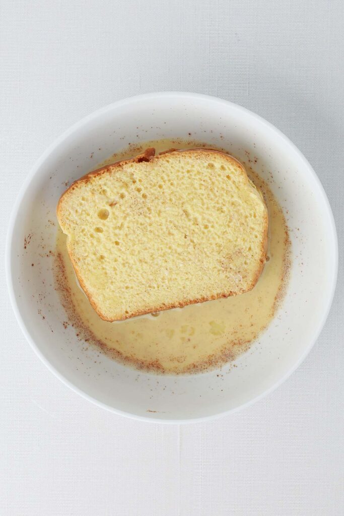 Top down image showing a small white bowl filled with an egg mixture with bread soaking inside