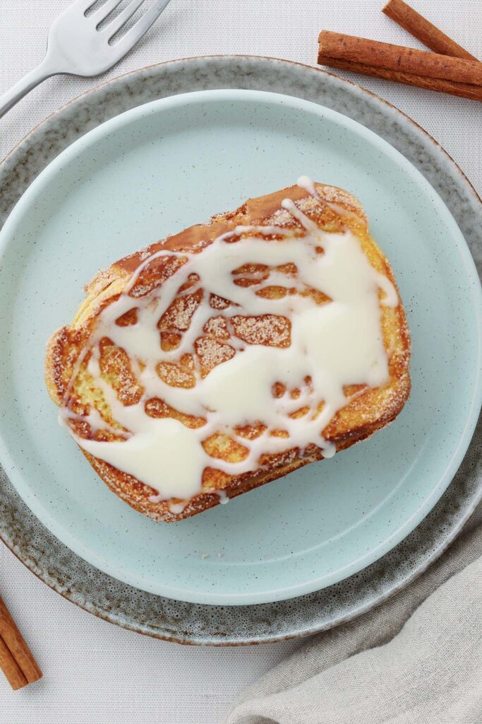 Top down image zoomed close to a french toast that has cinnamon and sugar plus a glaze. The french toast is sitting on a light blue plate.