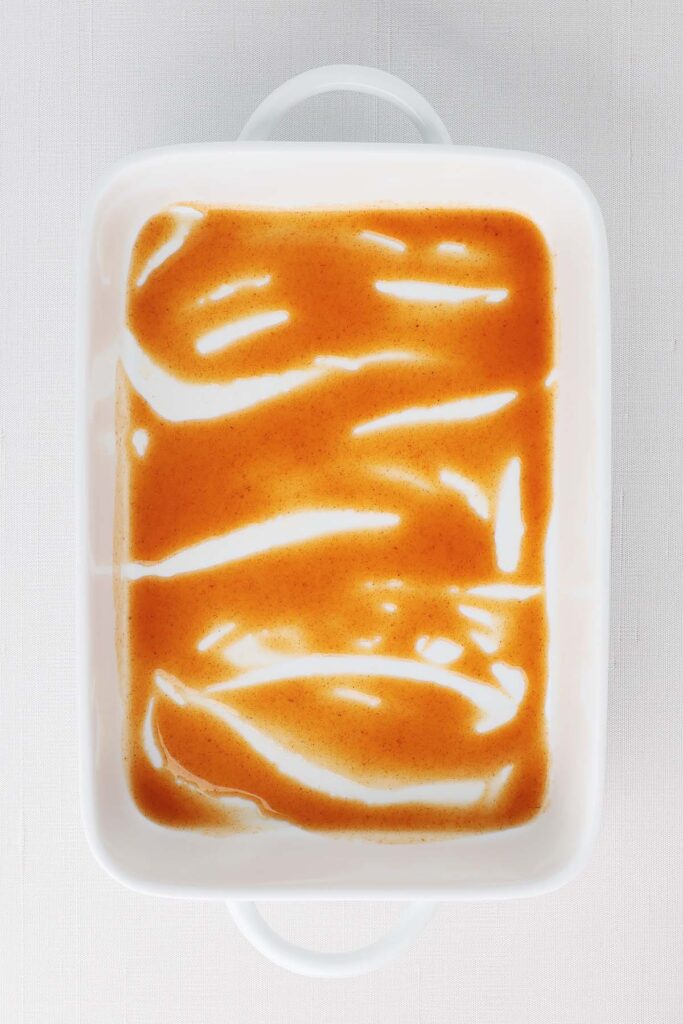 Top down image showing a white baking pan filled with enchilada sauce