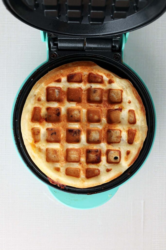 Top down showing the inside of the waffle maker with a crispy golden waffle insisde