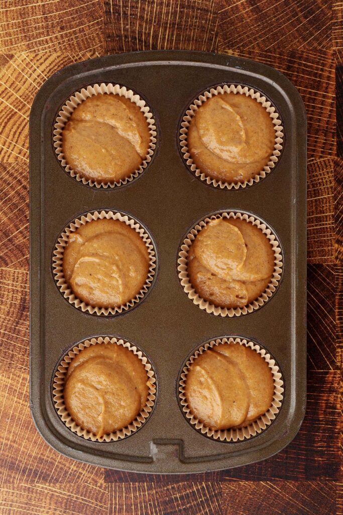Top down image showing a six cup cupcake pan filled with paper liners and cake mix