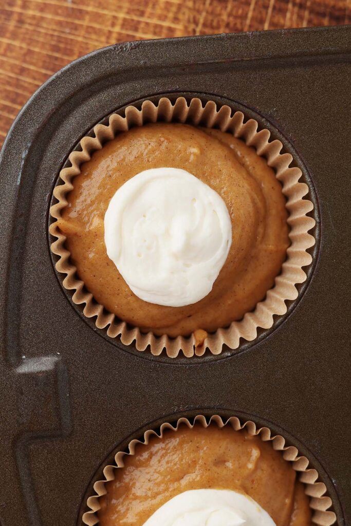 Top down image showing paper cupcake liners inside of a cake pan filled with cake batter and a dollop of a cream cheese mix