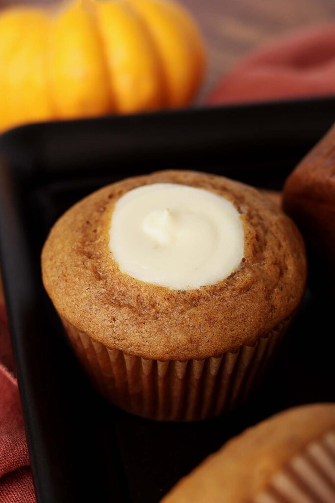 Close up image of a pumpkin muffin with a dollop of cream cheese filling right in the middle