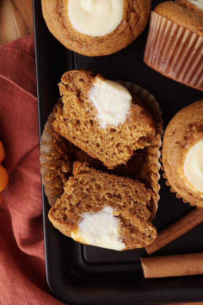 Top down image showing a pumpkin muffin that has been sliced in half and is sitting inside the liner. There is a cream cheese filling iniside.