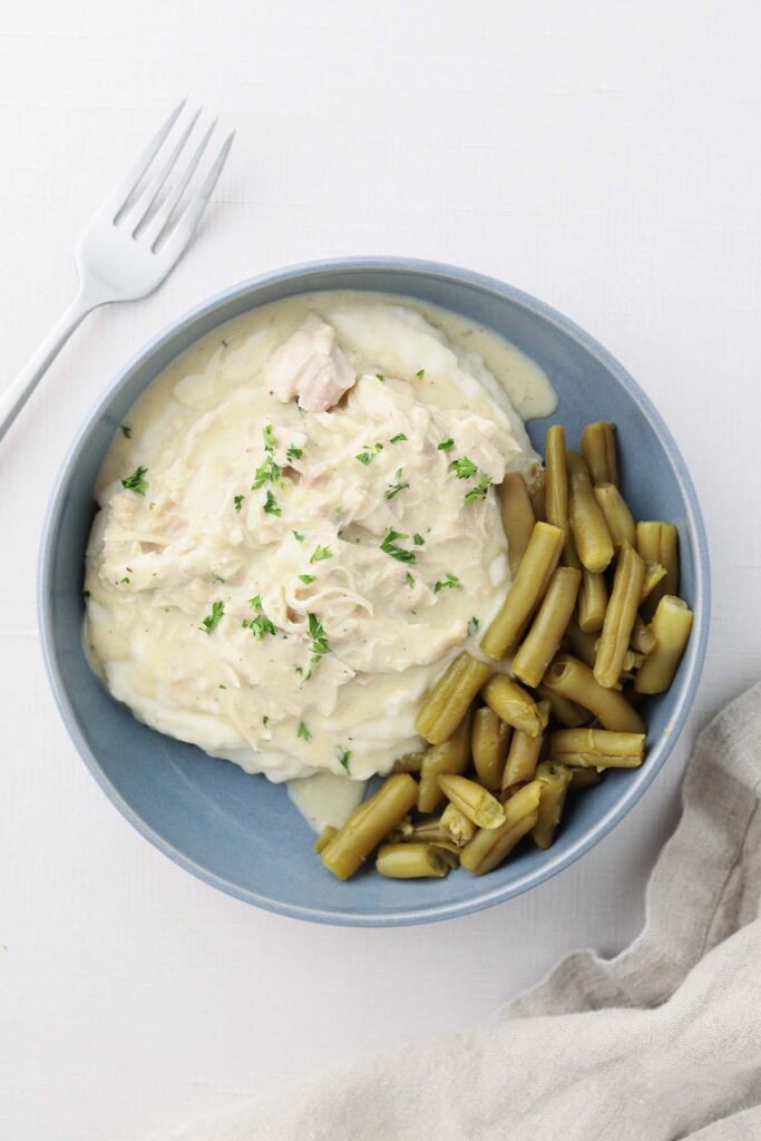 Top down image showing a blue shallow bowl filled with mashed potatoes and chicken gravy with green beans
