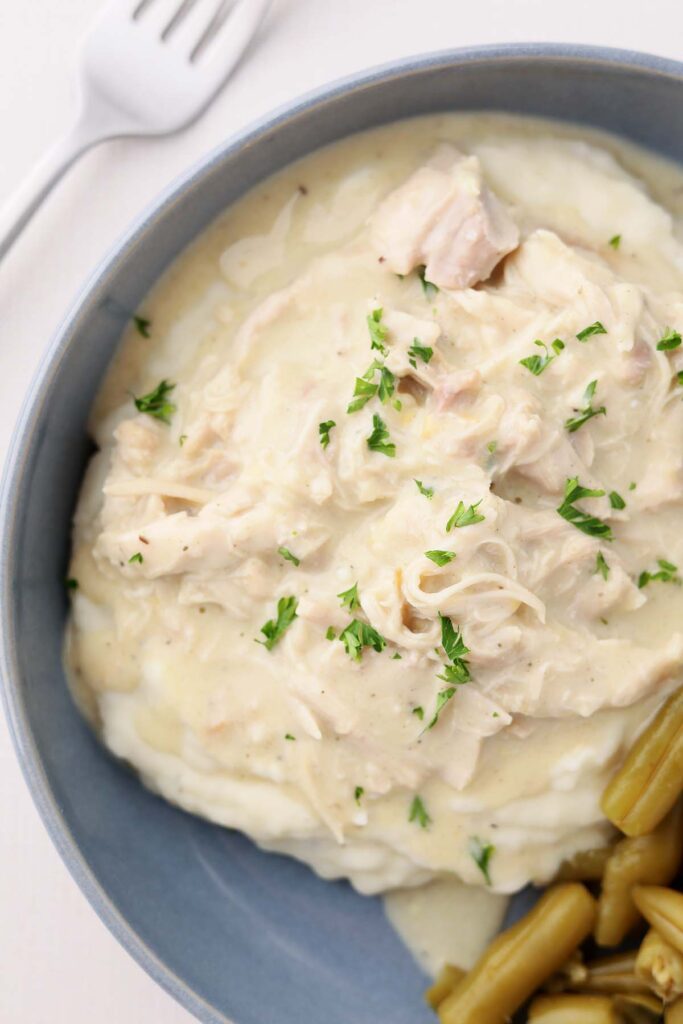 Top down image showing a blue shallow bowl filled with mashed potatoes and chicken gravy with green beans